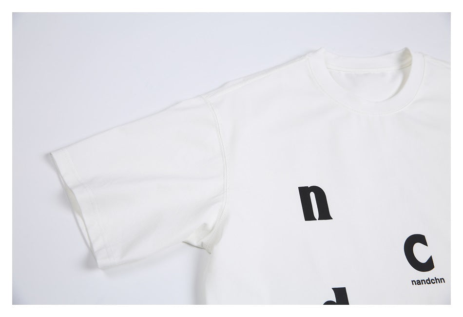 Partial flat lay of a white short-sleeve T-shirt with scattered black lettering.