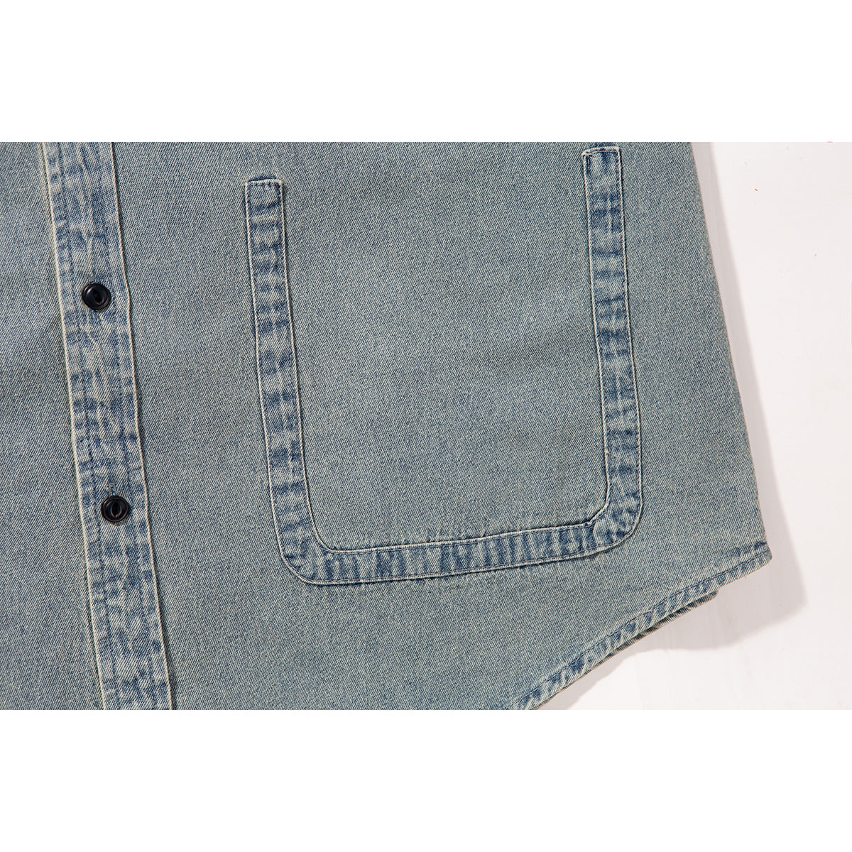 Close-up of a large patch pocket and black buttons on a light blue denim shirt.
