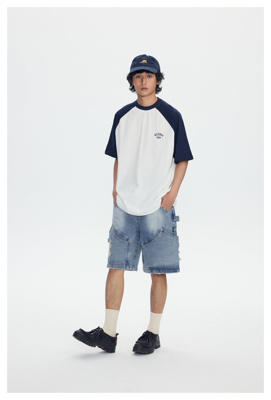 Full-length front view of a model wearing a white raglan T-shirt with navy sleeves and light blue denim shorts.