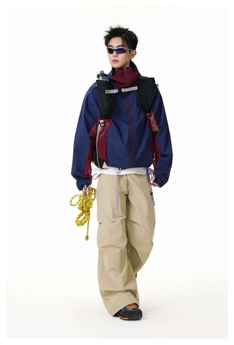 Model wearing a navy hooded jacket with burgundy panels and loose beige trousers, shown from the front.