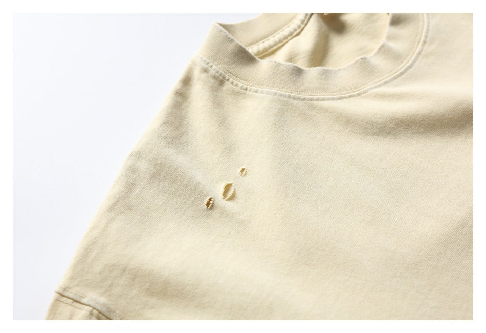 Close-up of the pale cream T-shirt’s crew neckline and shoulder, showing three small distressed holes.