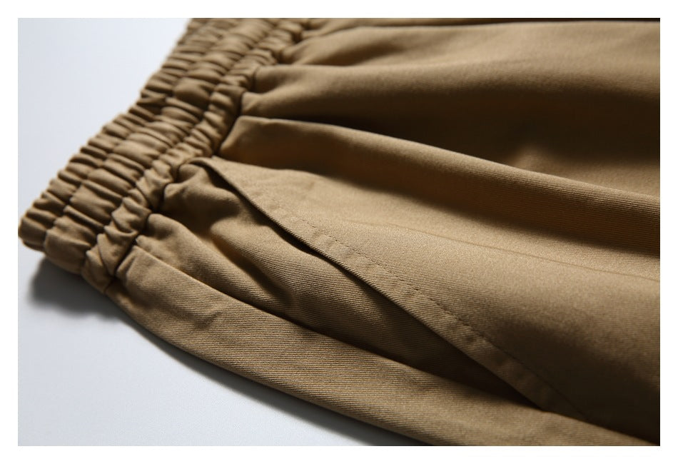 Close-up of tan trousers showing the elastic waistband, side pocket opening and stitching.