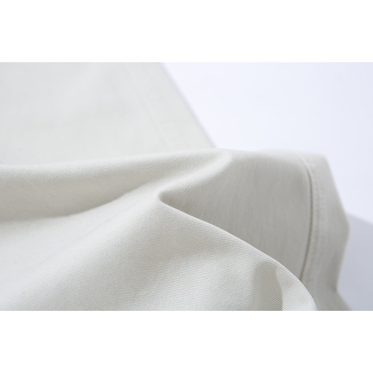Close-up of the fine diagonal texture and stitching on ivory trouser fabric.