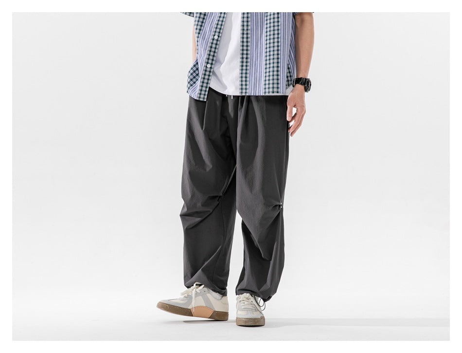 Angled front view of a cropped model wearing loose charcoal-gray trousers with gathered knee details.