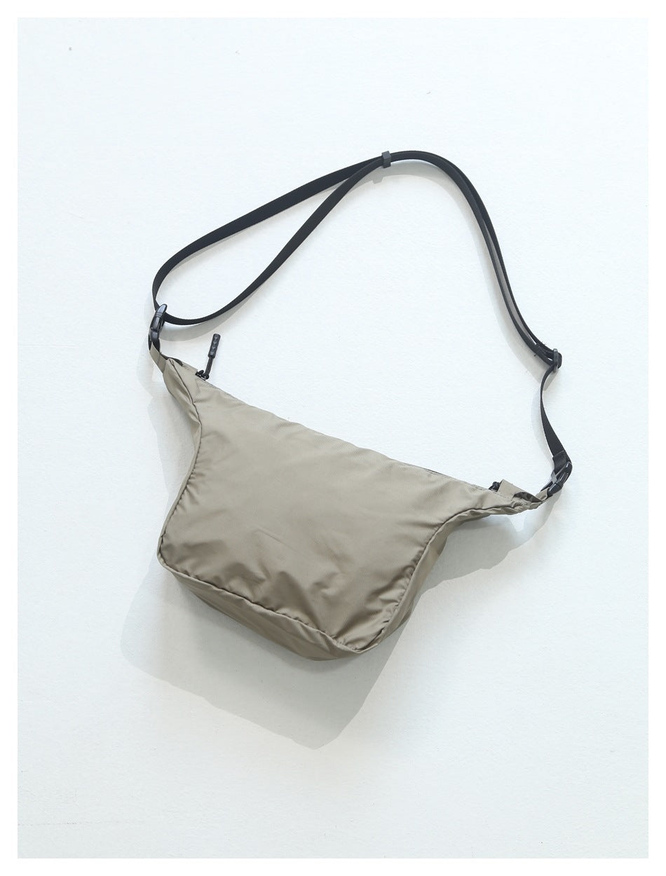 Taupe crossbody bag with a wide black adjustable strap, shown against a white background.