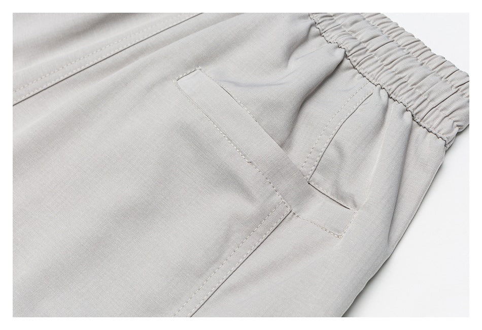 Close-up of light gray trousers showing an elastic waistband and angled pocket with stitched seams.