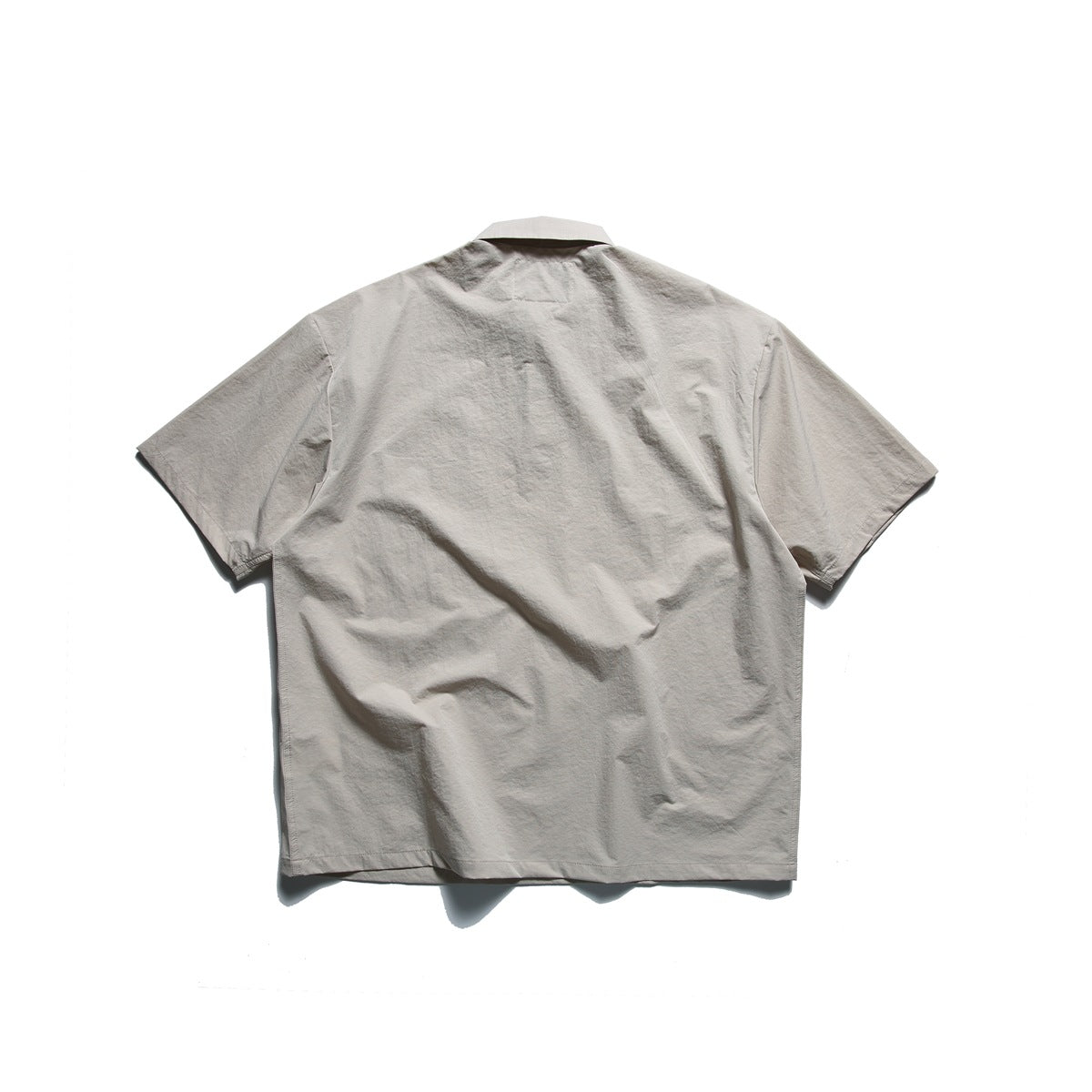 Back view of a light taupe short-sleeve collared shirt on a white background.