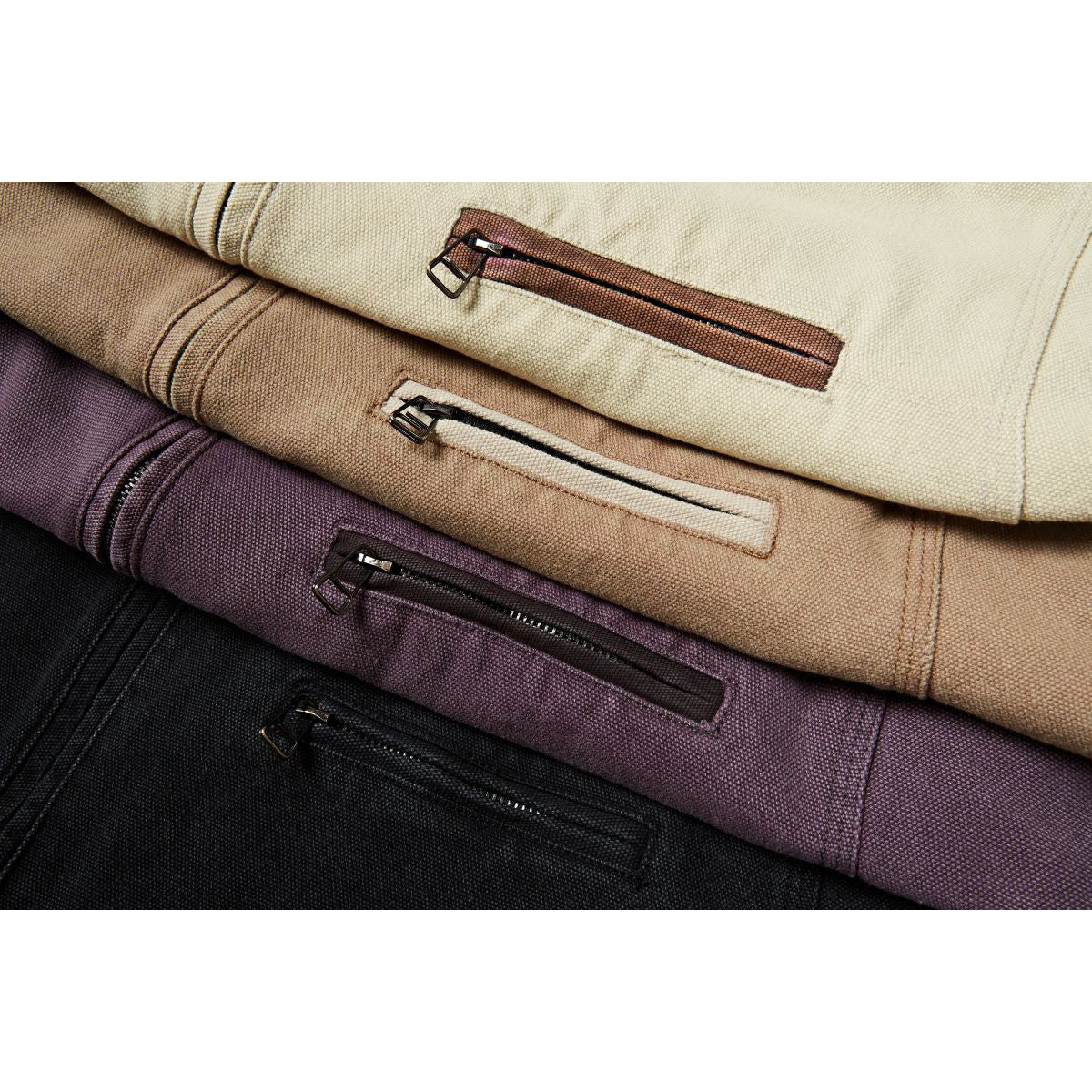 Close-up of four jackets in cream, tan, plum, and black, showing their zippered chest pockets.