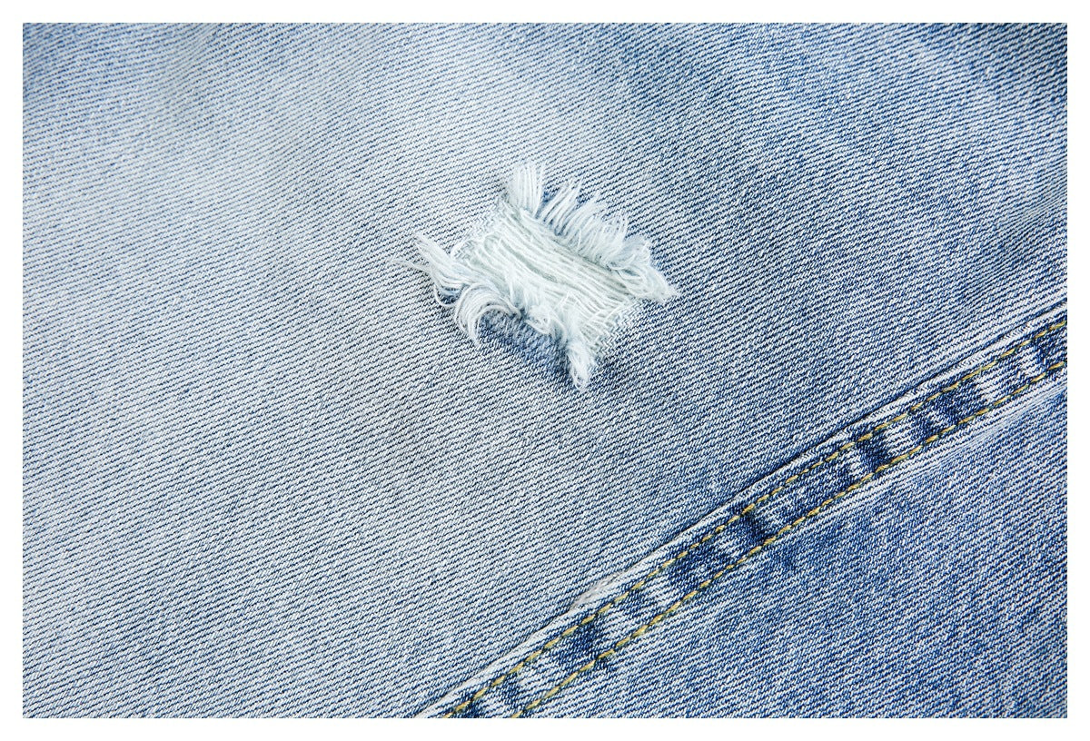 Close-up of light blue denim with a frayed distressed spot and diagonal yellow stitching.