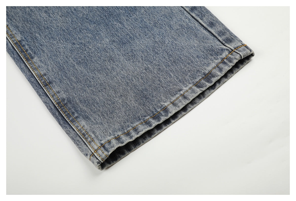 Close-up of a faded blue denim jeans leg hem with golden stitching.