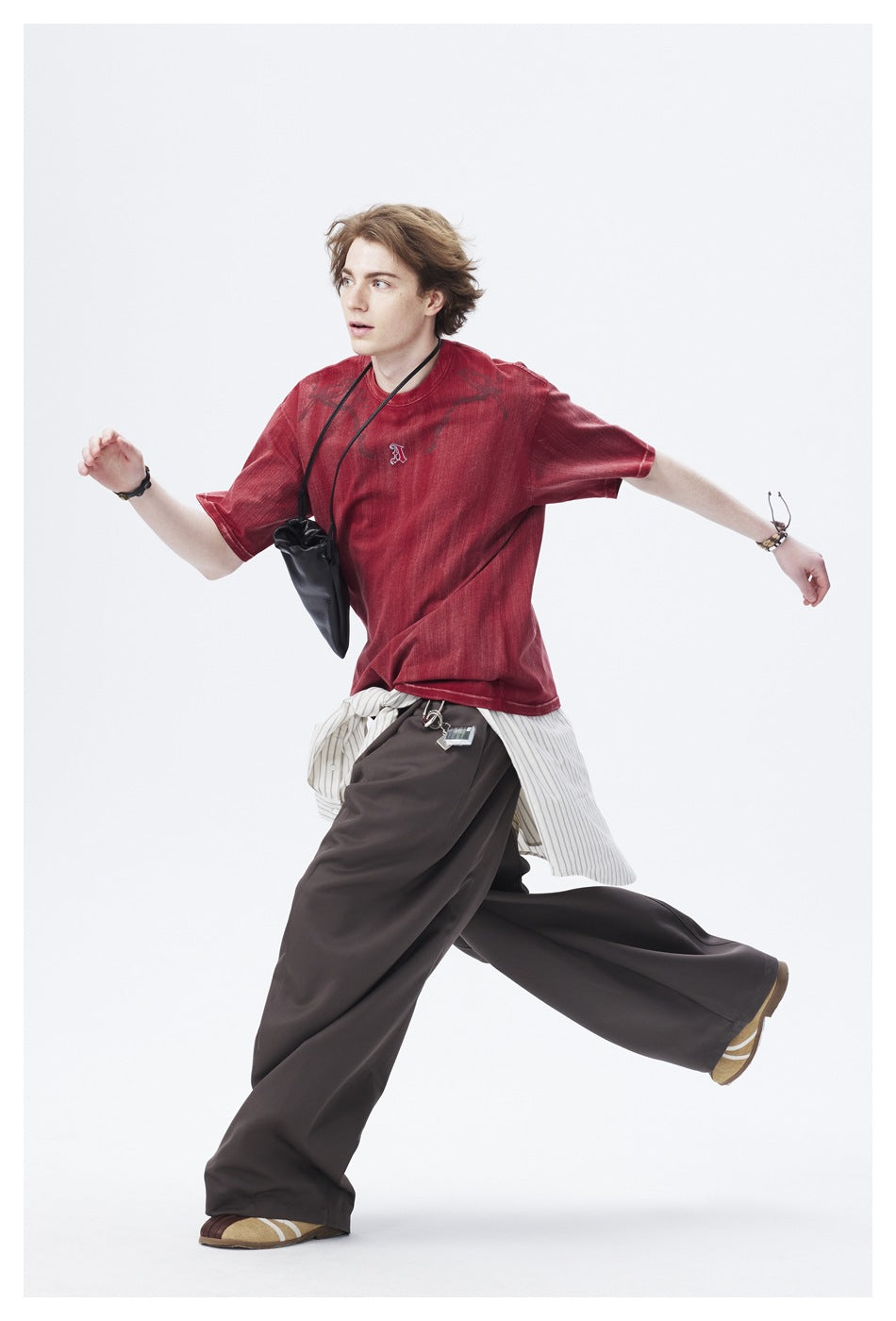 Model wearing a faded red graphic T-shirt and loose dark trousers, captured in a running pose.
