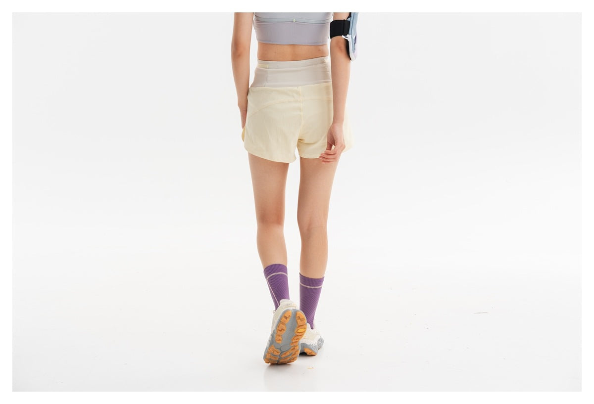 Rear view of a model wearing cream running shorts with a high waistband.