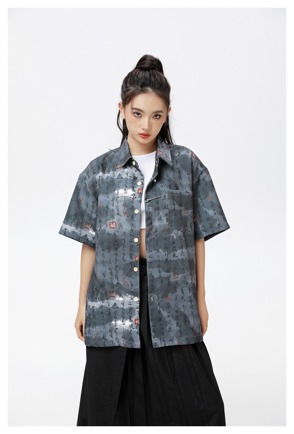 Close-up of a model wearing the black-gray calligraphy-print short-sleeve shirt open over a white top, showing pocket and