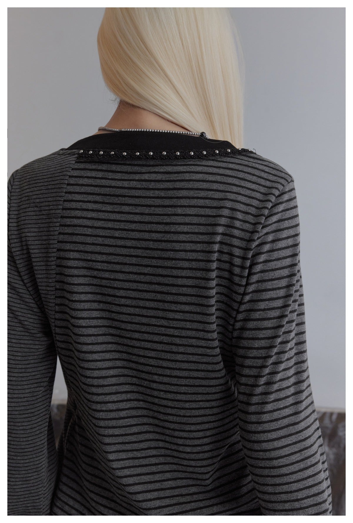 Back view of a model wearing a charcoal striped long-sleeve top with a black neckline and studded trim.