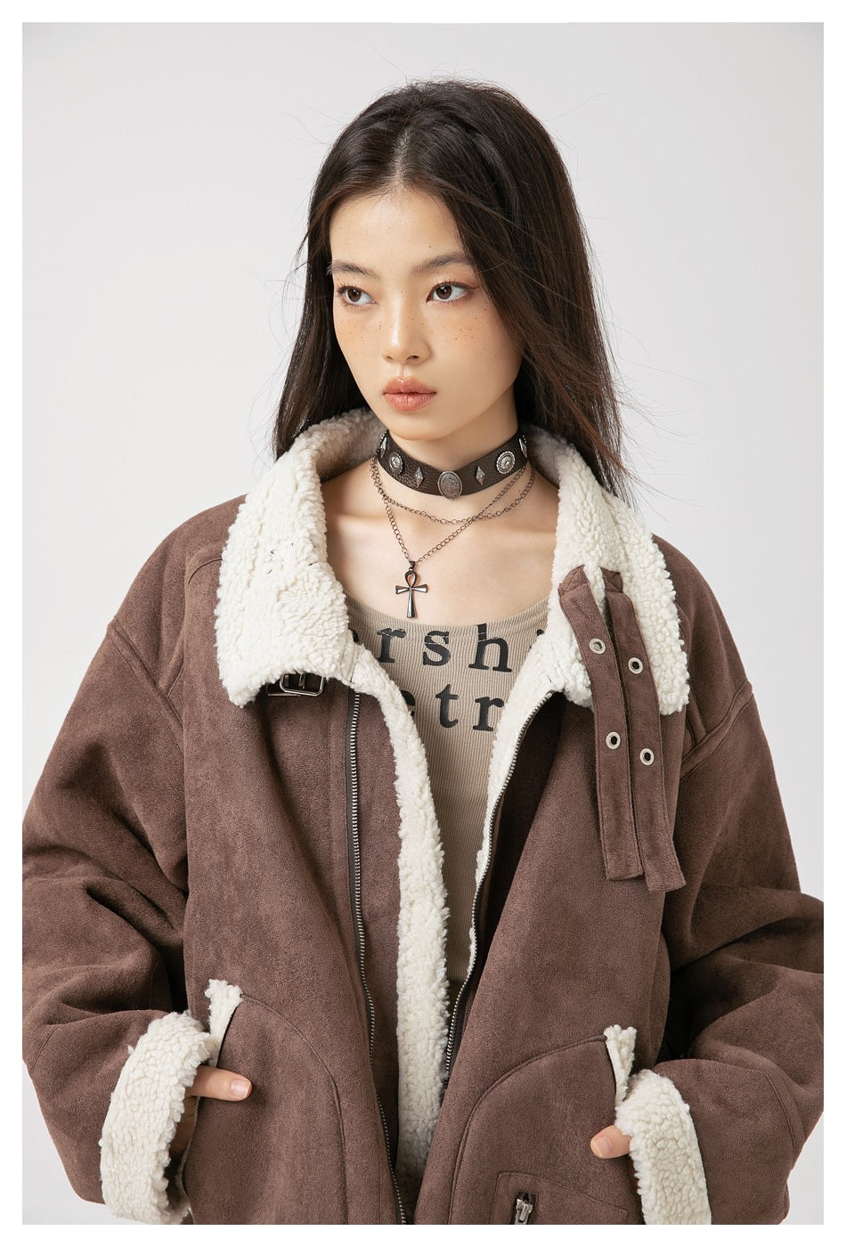 Close view of a model wearing a brown jacket with a cream sherpa collar, lining and cuff trim.