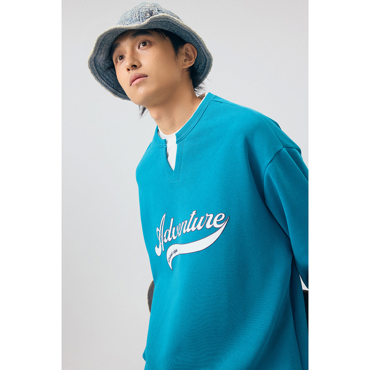 Close view of a teal sweatshirt with a notched neckline and white script chest graphic.