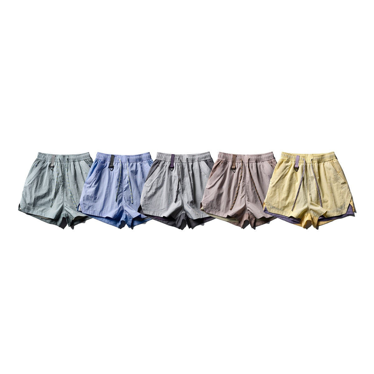 Five pairs of drawstring shorts shown side by side in pale gray-green, blue, gray, mauve and yellow.