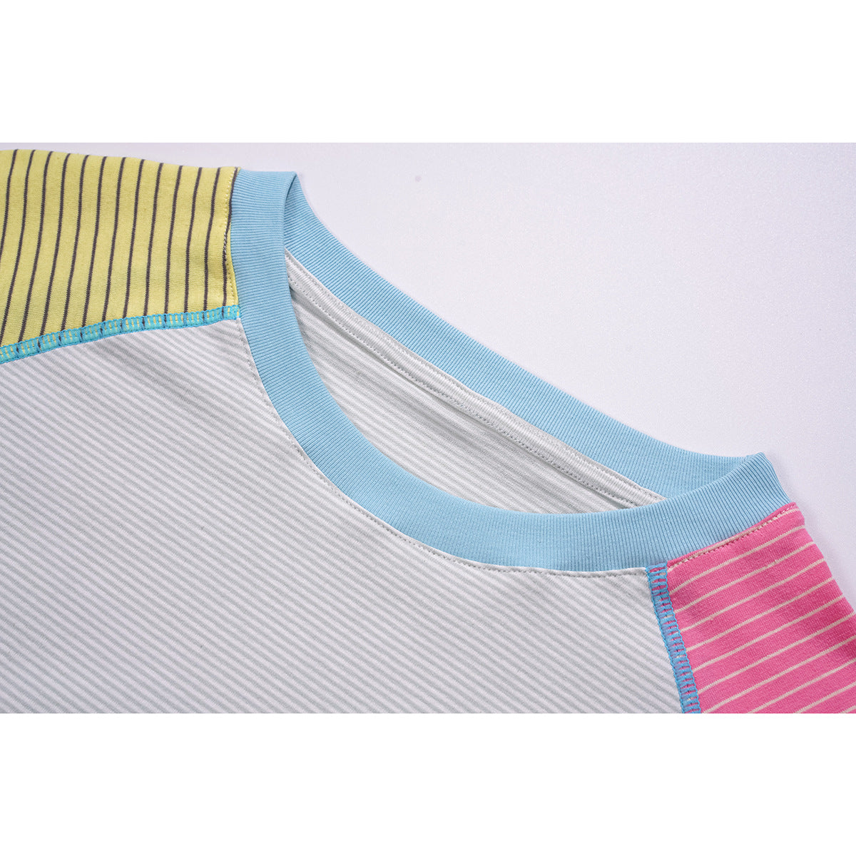 Close-up of a light gray raglan shirt neckline with a sky-blue ribbed collar and yellow and pink striped shoulder panels.