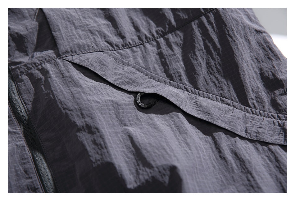 Close-up of a charcoal jacket flap pocket with a black ring pull and nearby zipper.