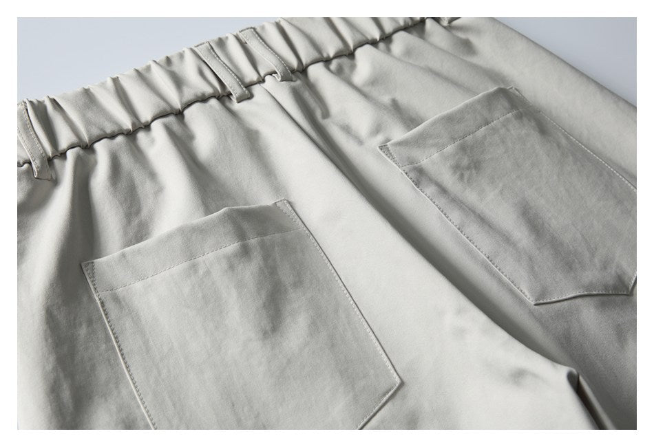 Close-up of light gray trousers showing an elastic waistband, belt loops, and two large patch pockets.