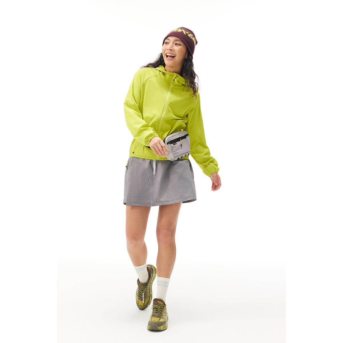 Woman wearing a bright lime hooded jacket, gray running skirt, and patterned burgundy beanie.