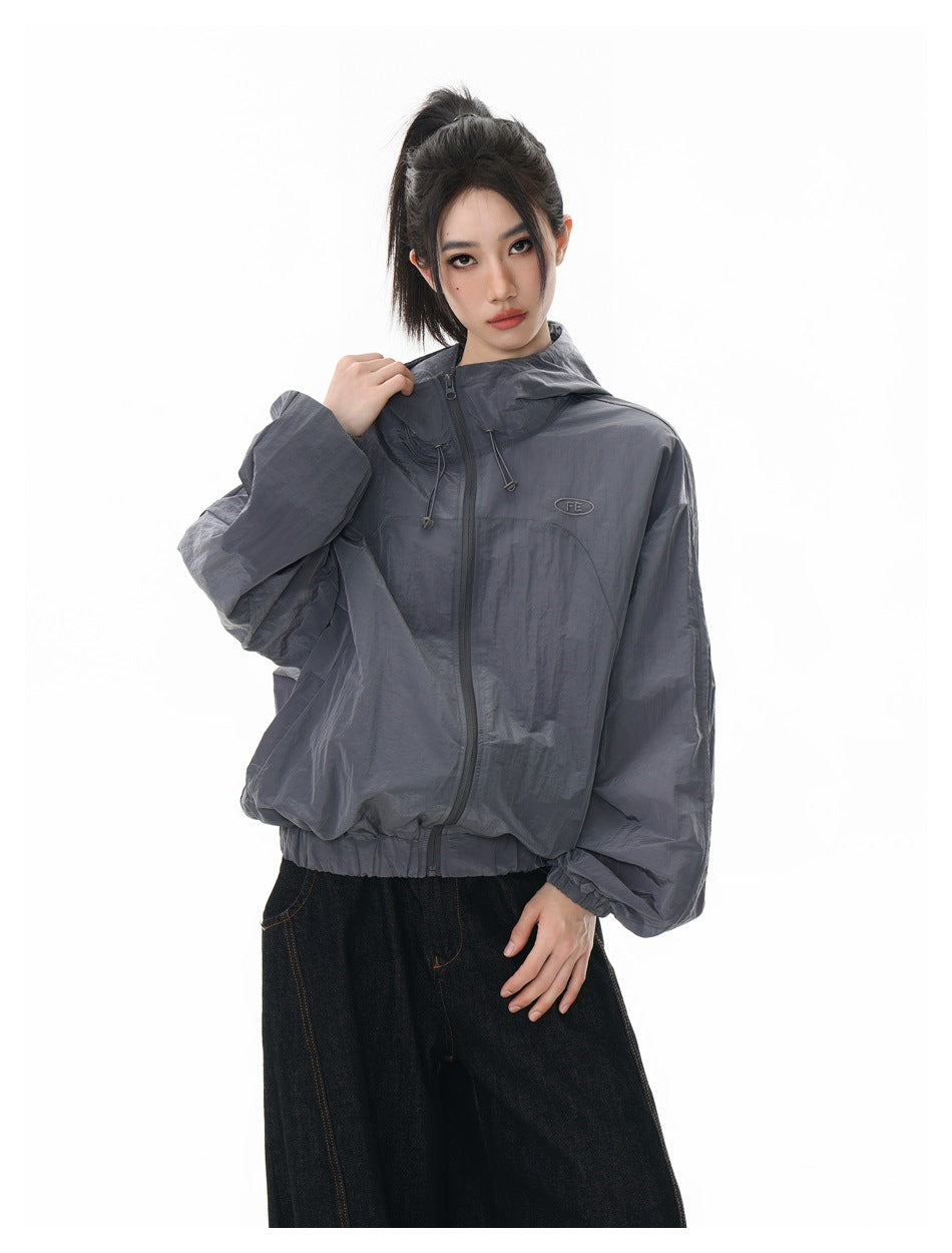 Model wearing a slate-gray hooded zip jacket with a small chest emblem, shown from the front.