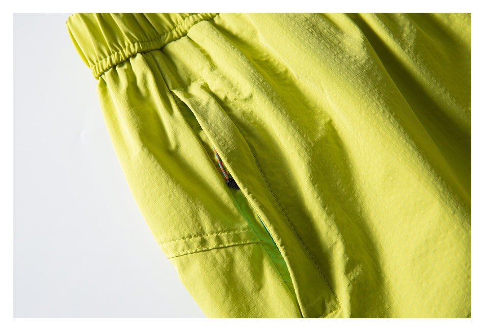 Close-up of a side pocket opening on lime-yellow shorts, with a small section of multicolored cord visible.