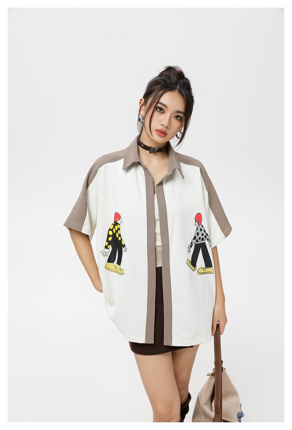 Model wearing an oversized ivory short-sleeve shirt with taupe trim and two colorful walking-figure prints.