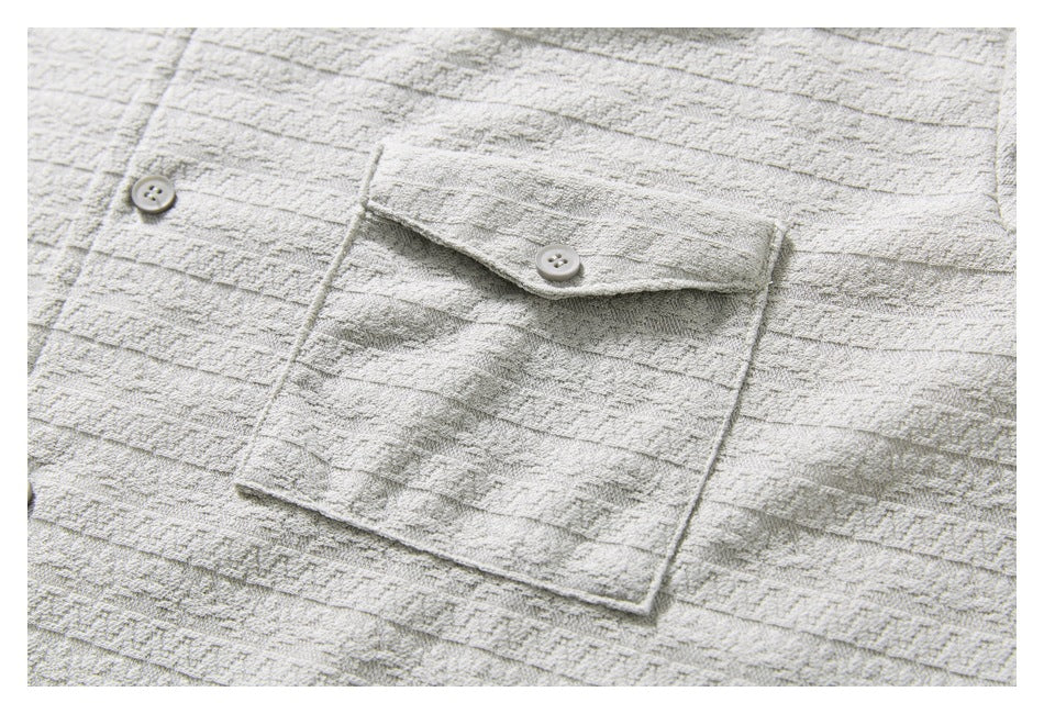 Close-up of a buttoned patch pocket on a light gray shirt with a raised geometric pattern.