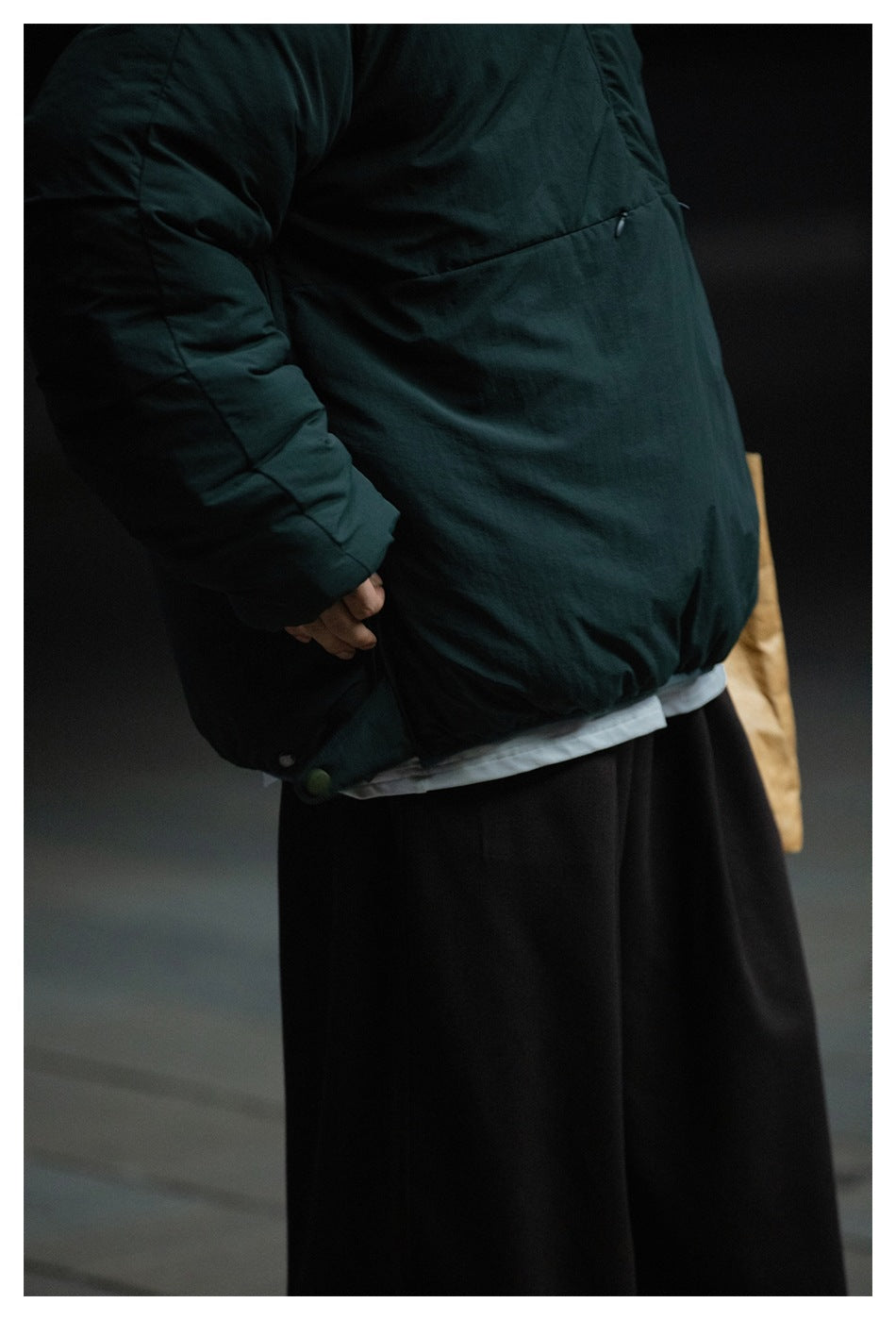 Close-up of the dark teal padded jacket showing its front pocket seam, sleeve, and adjustable hem.