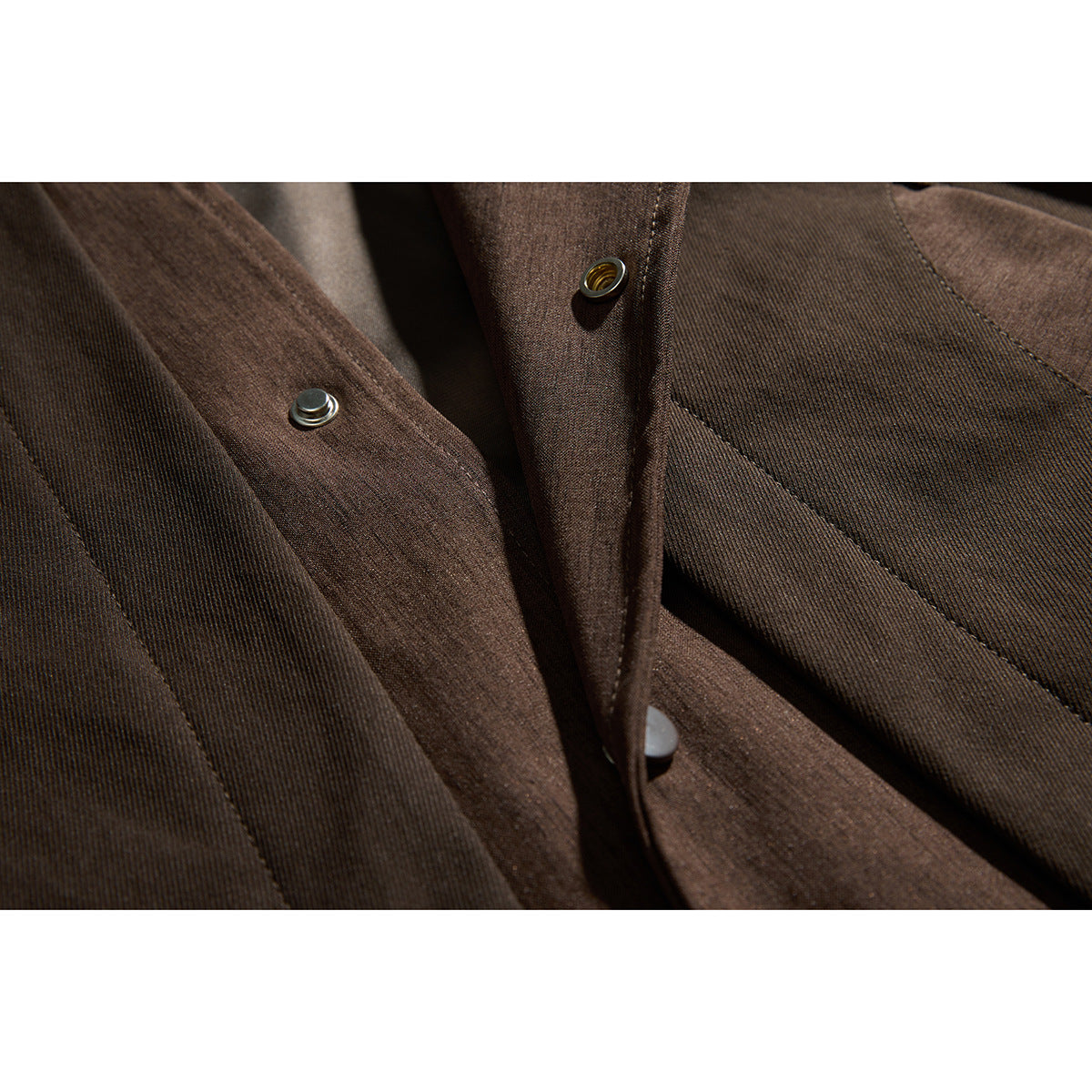 Close-up of dark brown jacket fabric and placket showing metal snap fasteners and stitching.