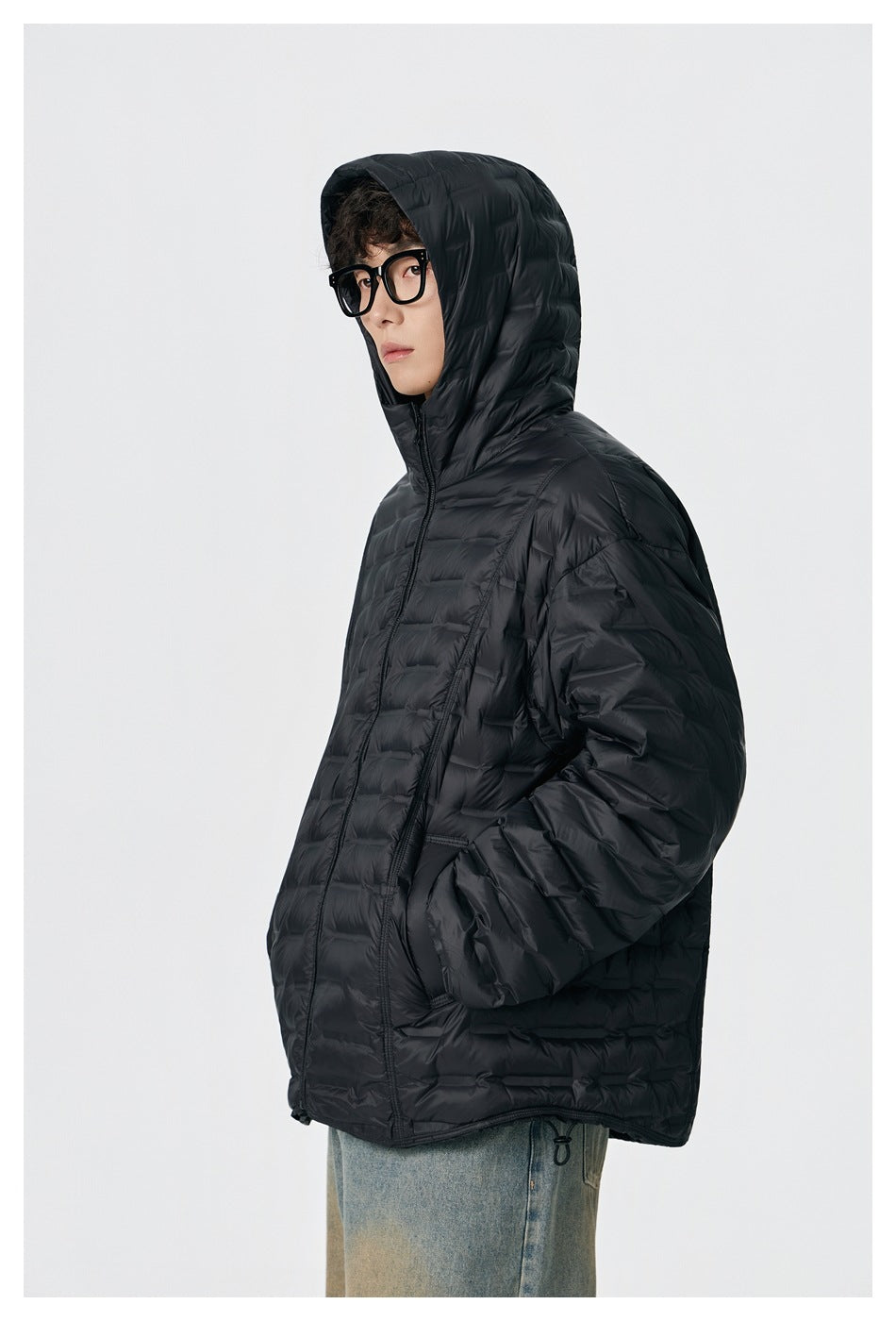 Close side view of a model wearing a black quilted jacket with the hood up.