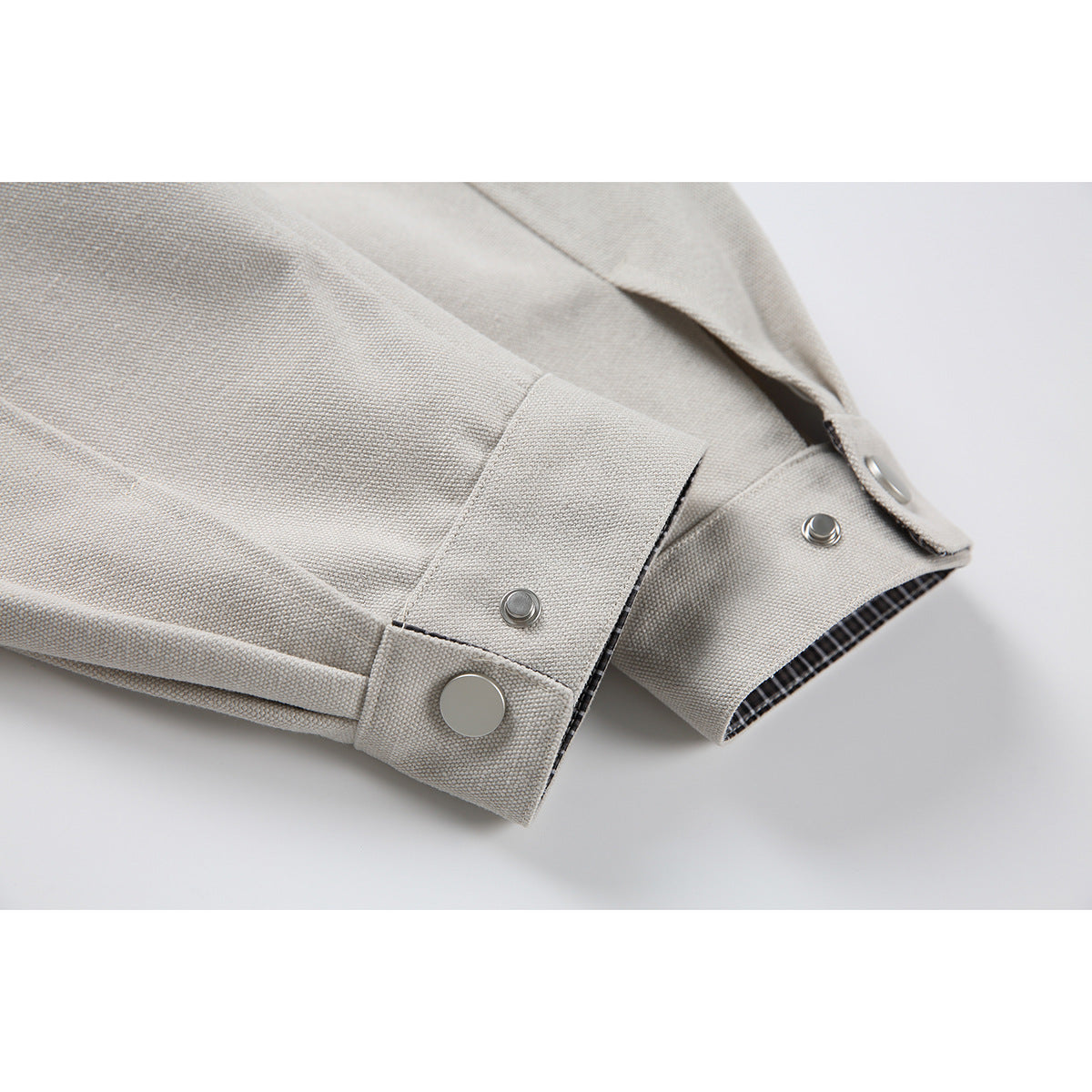 Close-up of a light beige jacket sleeve cuff with snap fasteners and a glimpse of checked lining.