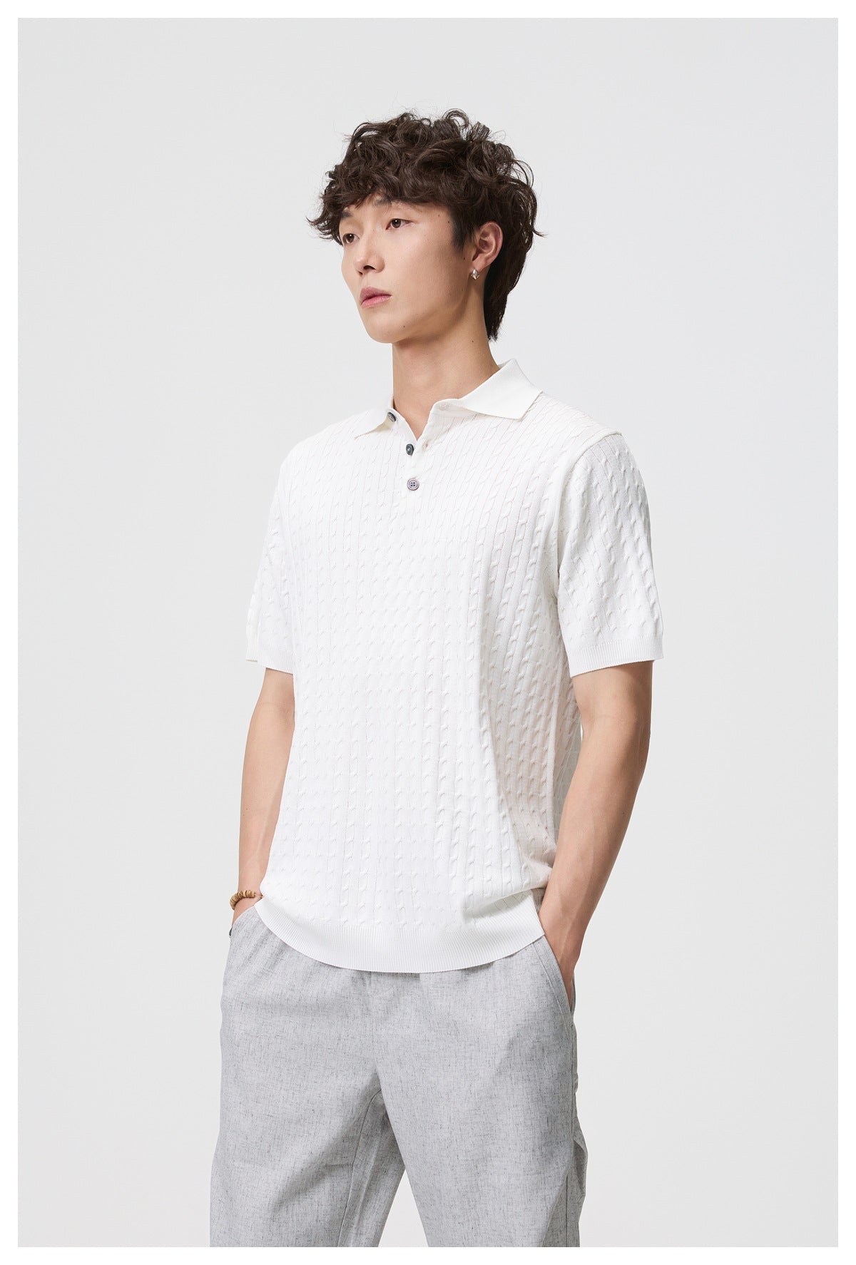 Three-quarter front view of a model wearing a white short-sleeve cable-knit polo and light gray trousers.