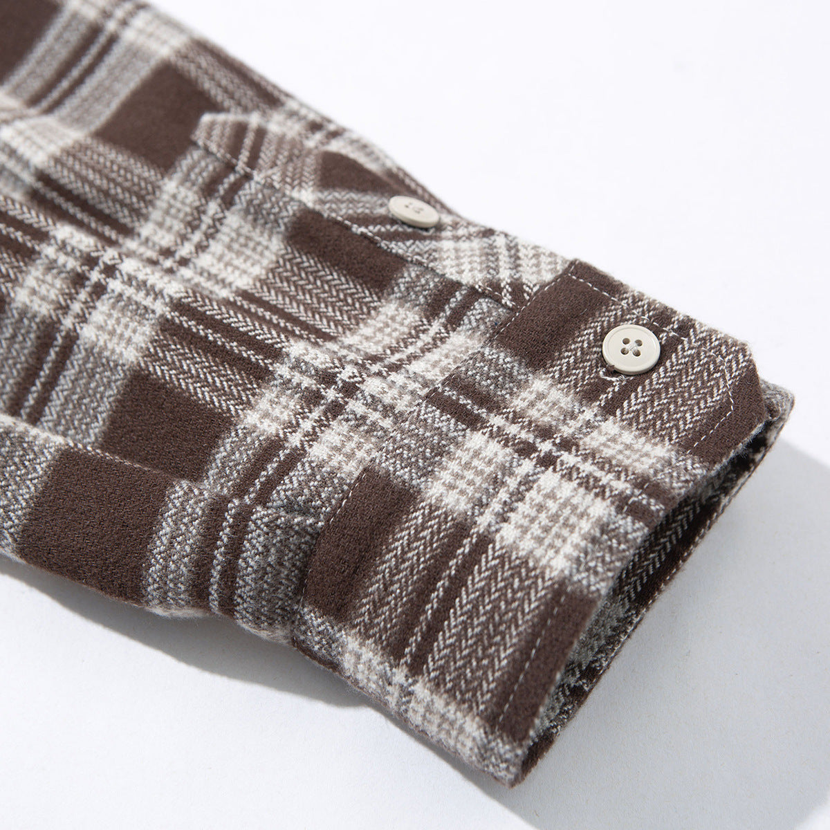 Close-up of a brown and cream plaid shirt cuff with two light-colored buttons.