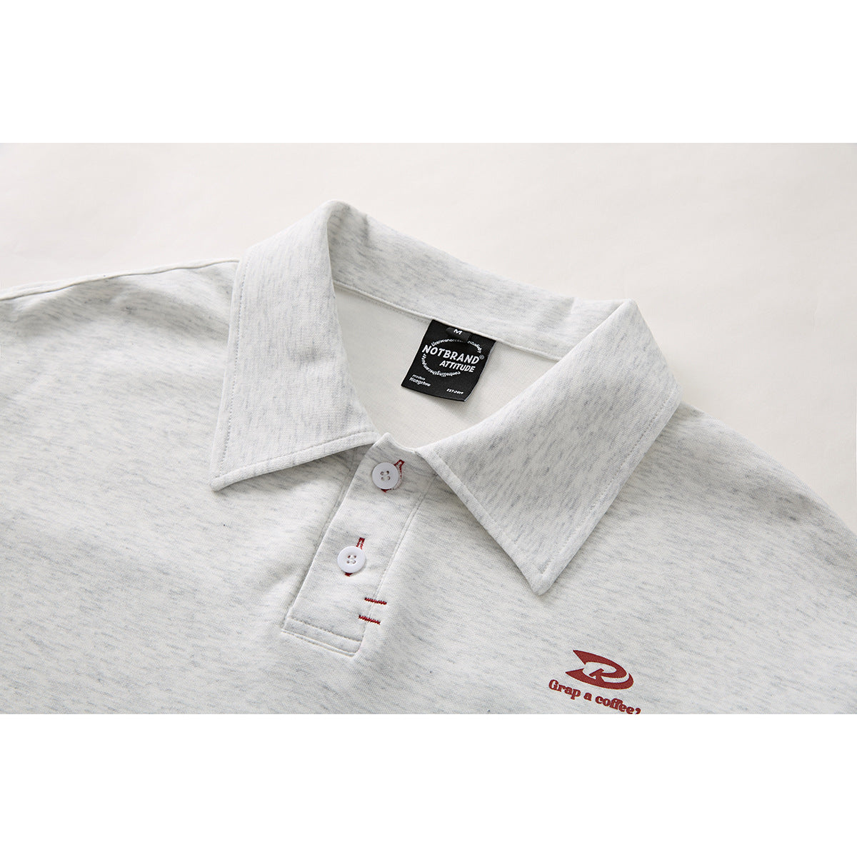 Close-up of a light gray heather polo shirt collar, two-button placket, and small red chest logo.