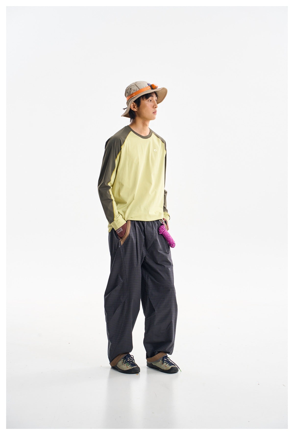 Side view of a model wearing a pale yellow and dark olive raglan shirt with loose charcoal plaid pants.