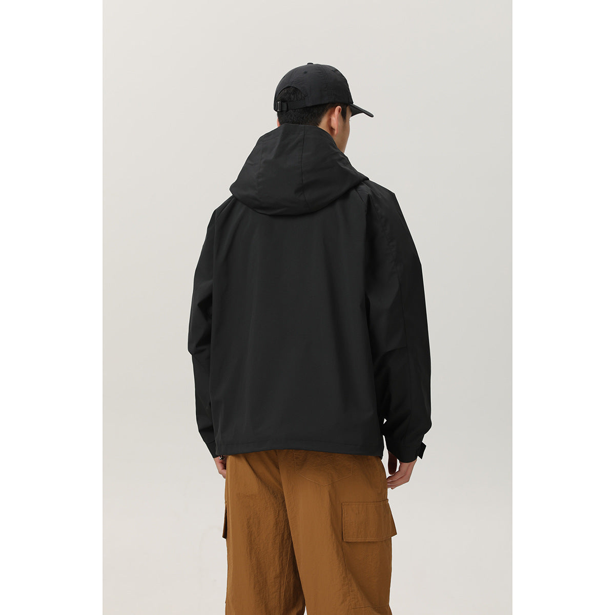 Back view of a model wearing a black hooded jacket with a plain back and brown cargo trousers.
