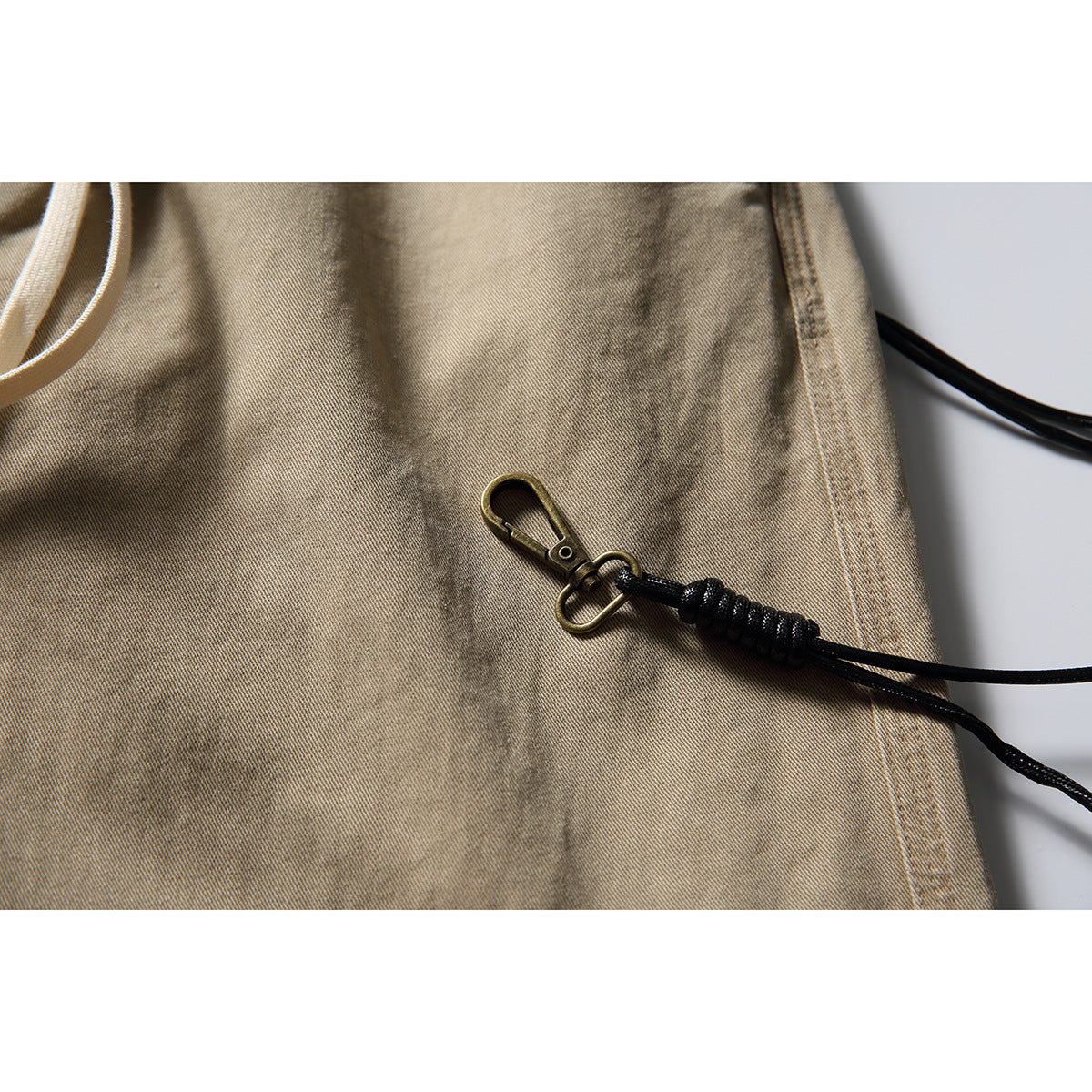 Close-up of a brass-tone clip and black cord attached to tan trouser fabric.