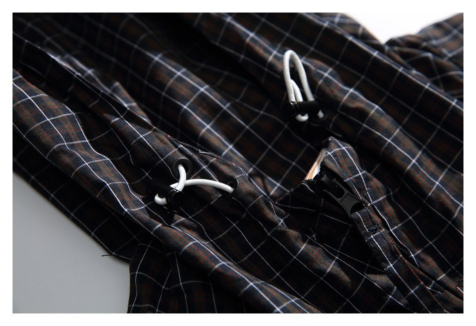 Close-up of white drawcords, black cord locks, and a buckle on the dark plaid jacket.