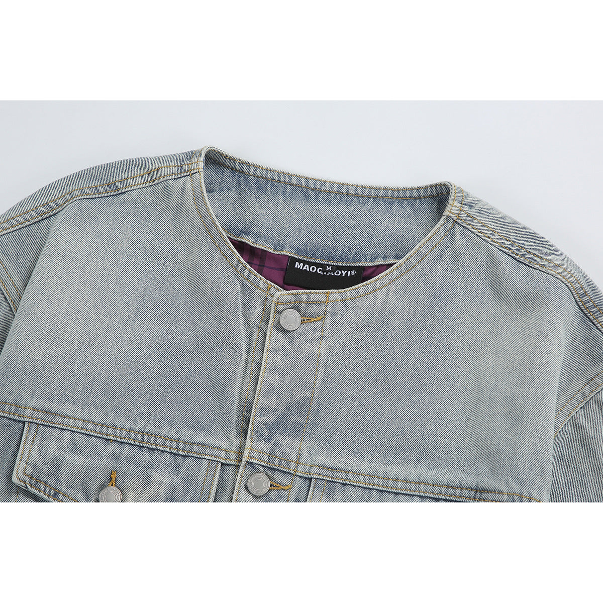Close-up of a light-wash denim jacket’s round neckline, metal buttons, and stitched seams.