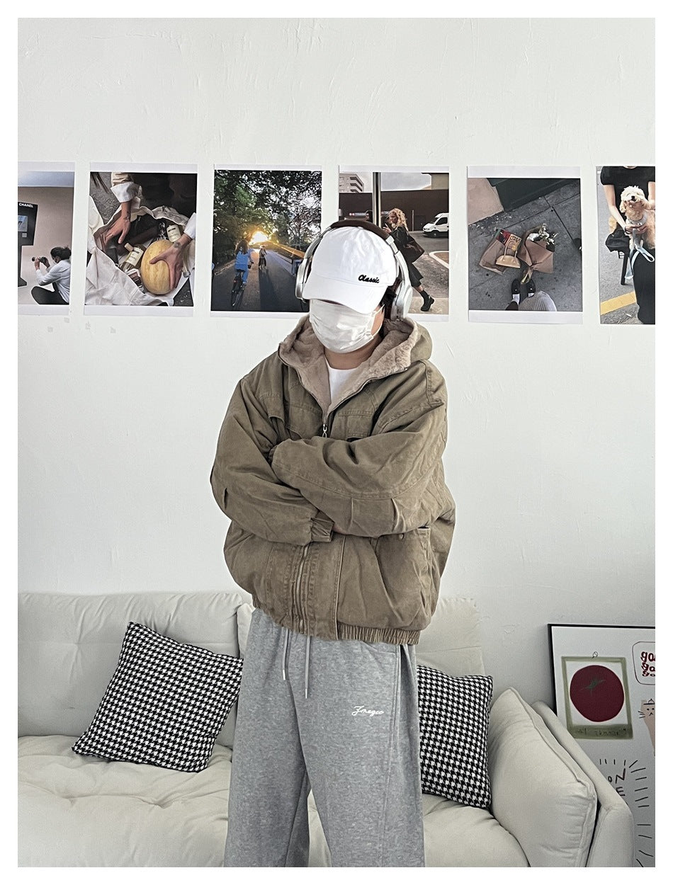 Person wearing khaki hooded jacket with fleece-like hood lining, arms crossed, with gray sweatpants and white cap