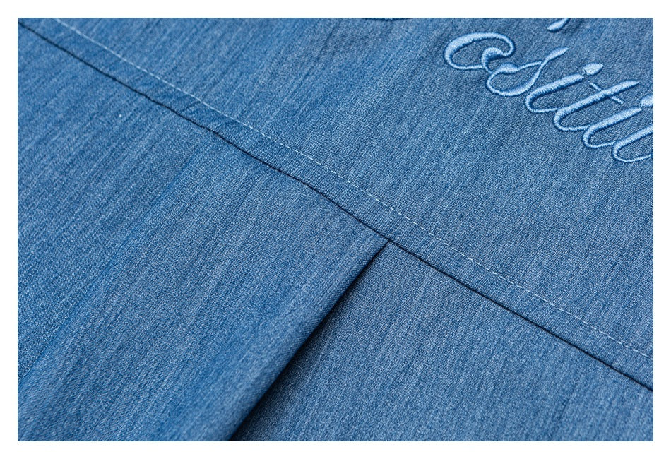 Blue denim close-up showing a stitched seam and part of light-colored embroidery.