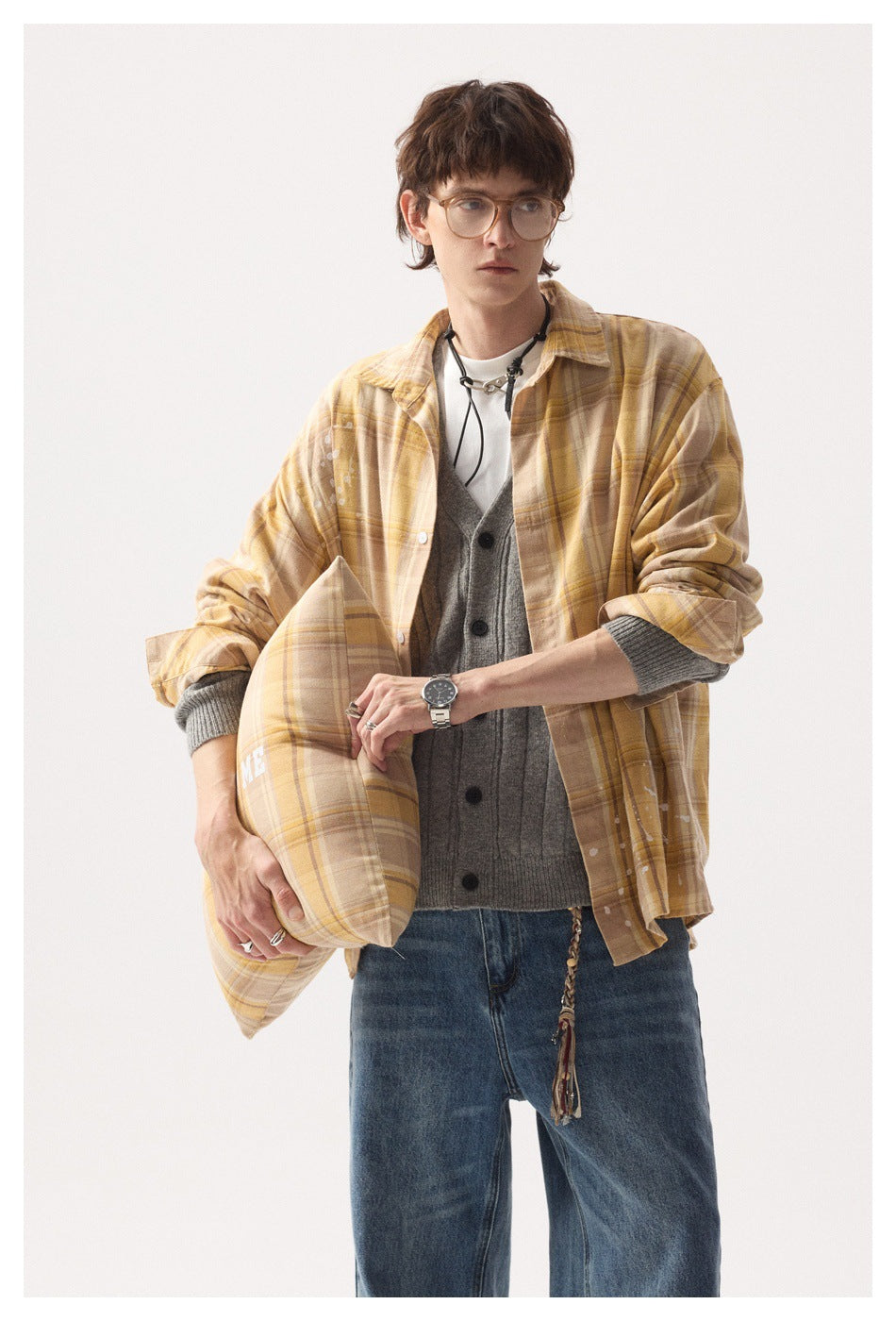 Model wearing a tan plaid button-up shirt over a gray cardigan, holding a matching plaid cushion.