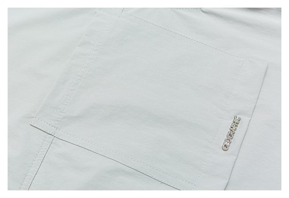 Close-up of the pale gray-green shirt's stitched rectangular panel and metal GEOGRAPHIC badge.