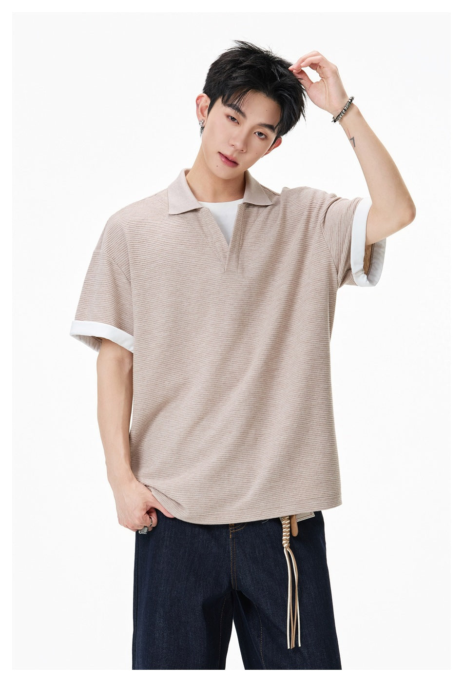 Model wearing a beige textured short-sleeve polo with a collar, open V-neck, and white turned-up cuffs.