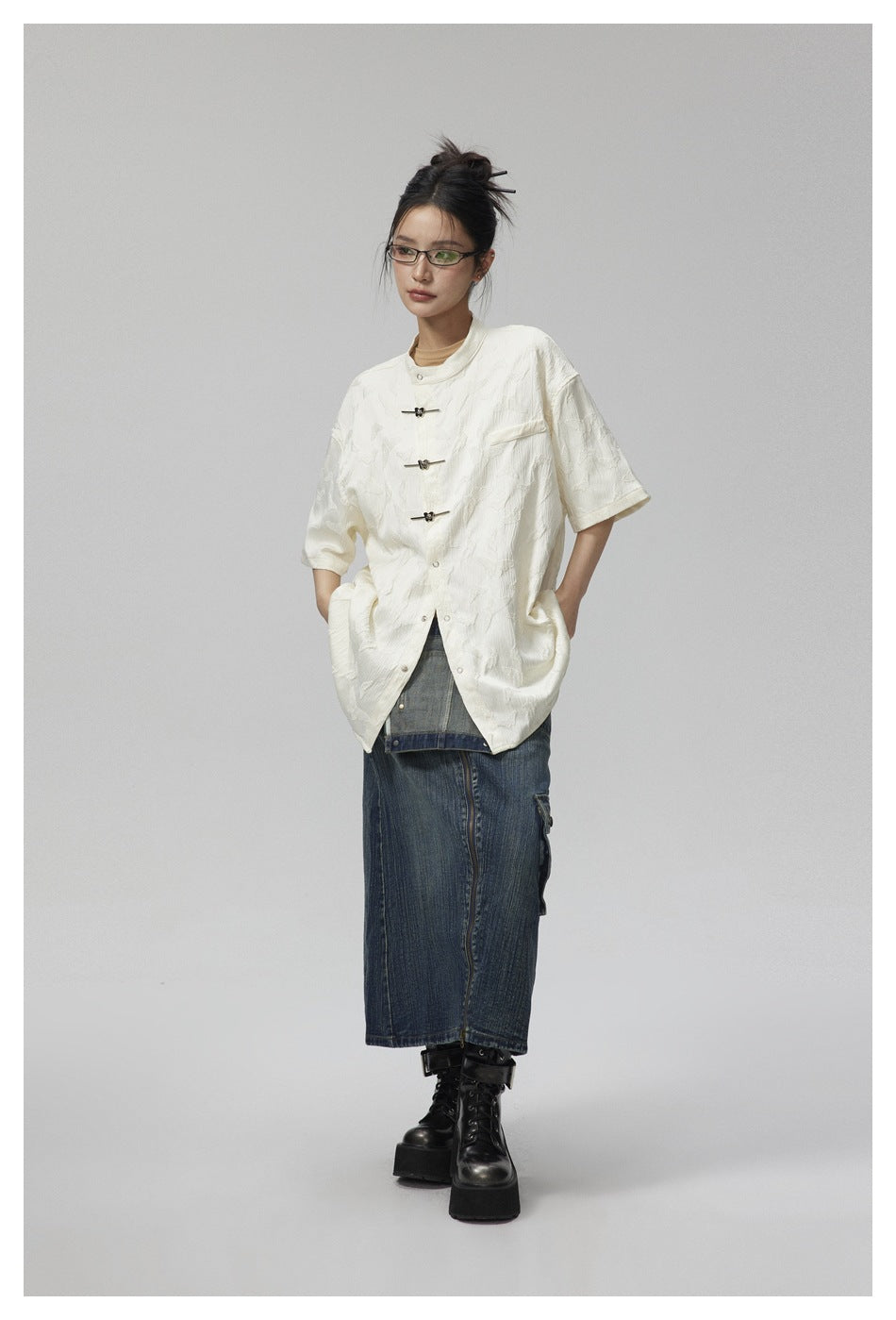 Full-length model wearing an ivory short-sleeve jacket with frog closures over a long denim skirt.