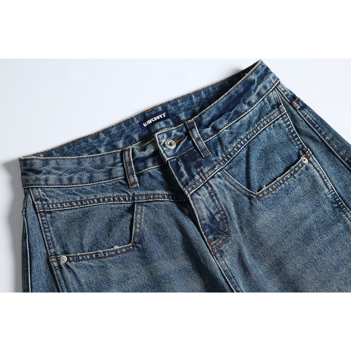 Close-up of the front waistband and pocket of blue-wash jeans with orange stitching and a metal button.