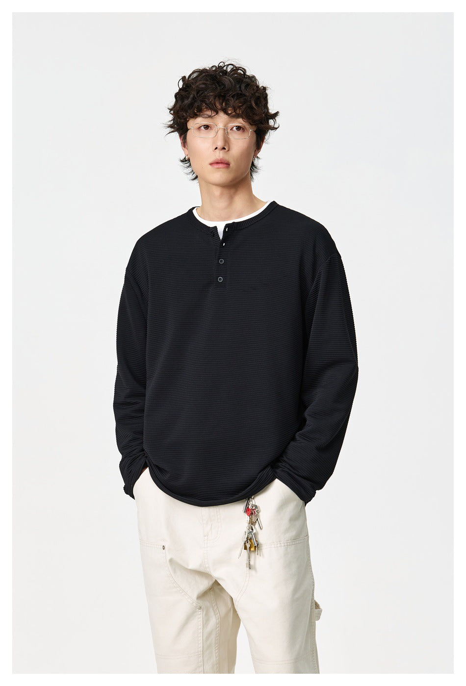 Front view of a model wearing a black ribbed long-sleeve henley with cream trousers.