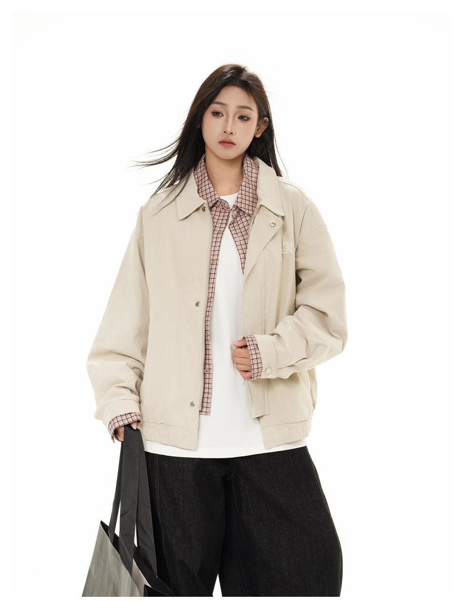 Model wearing a light beige collared jacket over a pink checked shirt and white top, with loose black jeans and a tote.